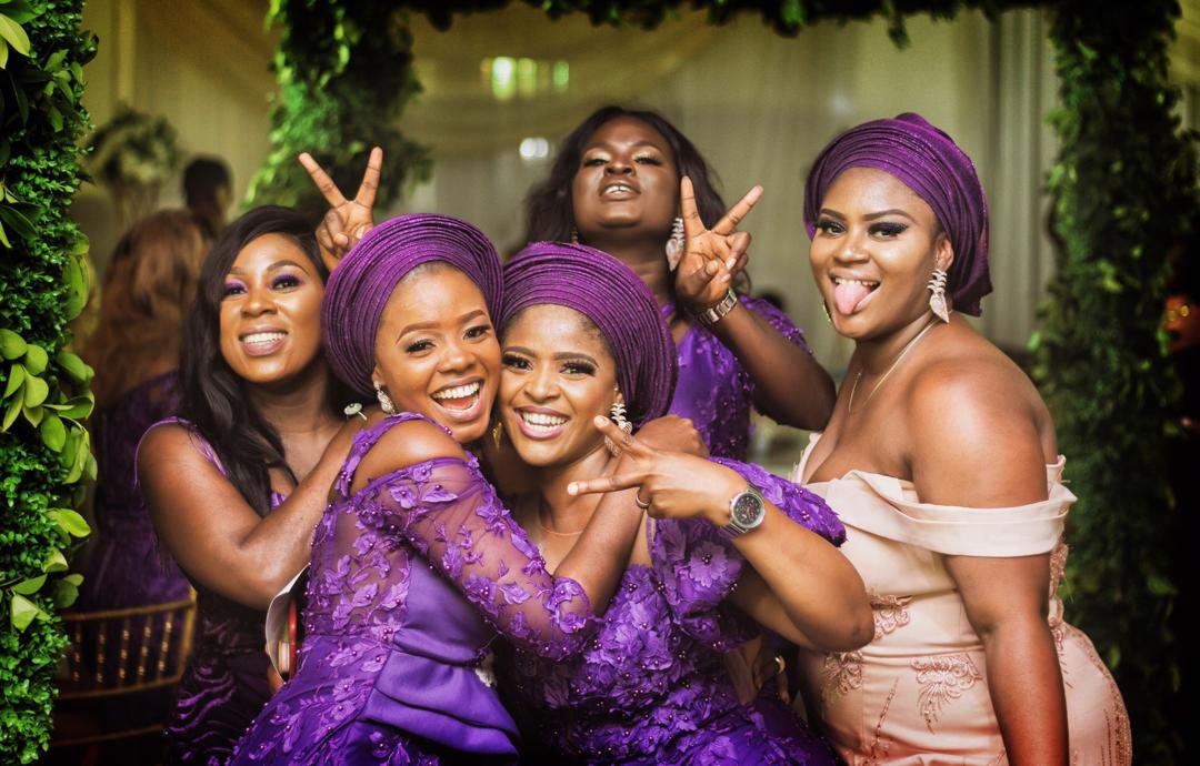 Vibrant Nigerian wedding guests in coordinated purple aso-ebi posing playfully for a group photo — capturing the fun, joy, and stress-free vibe of a well-planned event.